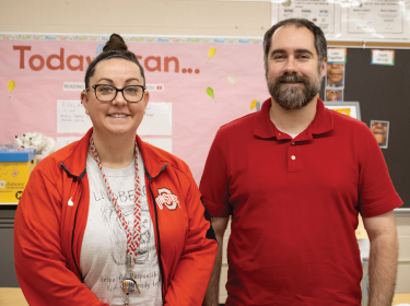 female teacher standing next to male teacher smiling at camera